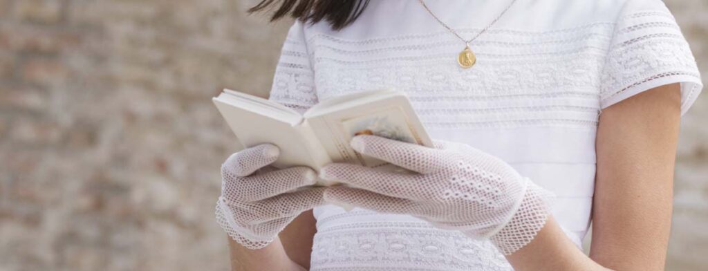 Niña vestida de blanco para celebrar su comunión leyendo un libro